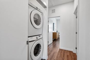 A white washer and dryer in a white laundry room with a wooden floor